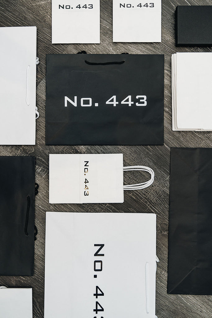 Black and white gift bags of various sizes sitting on a black wood table top for a women's clothing boutique
